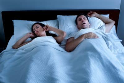 man snoring in his sleep while female partner covers her ears with her hands